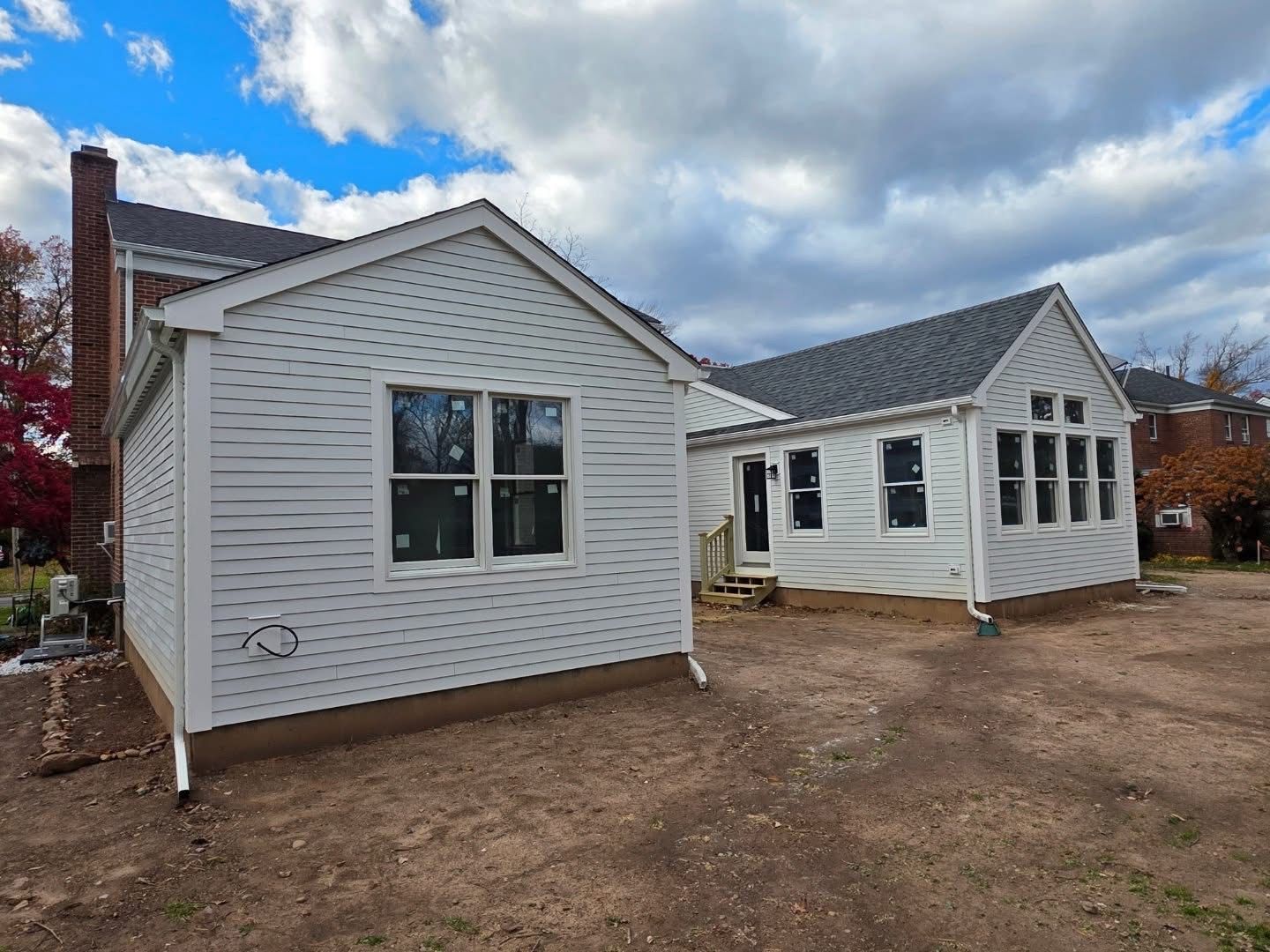 Exterior view of two white-sided house additions with new windows on a cloudy day.