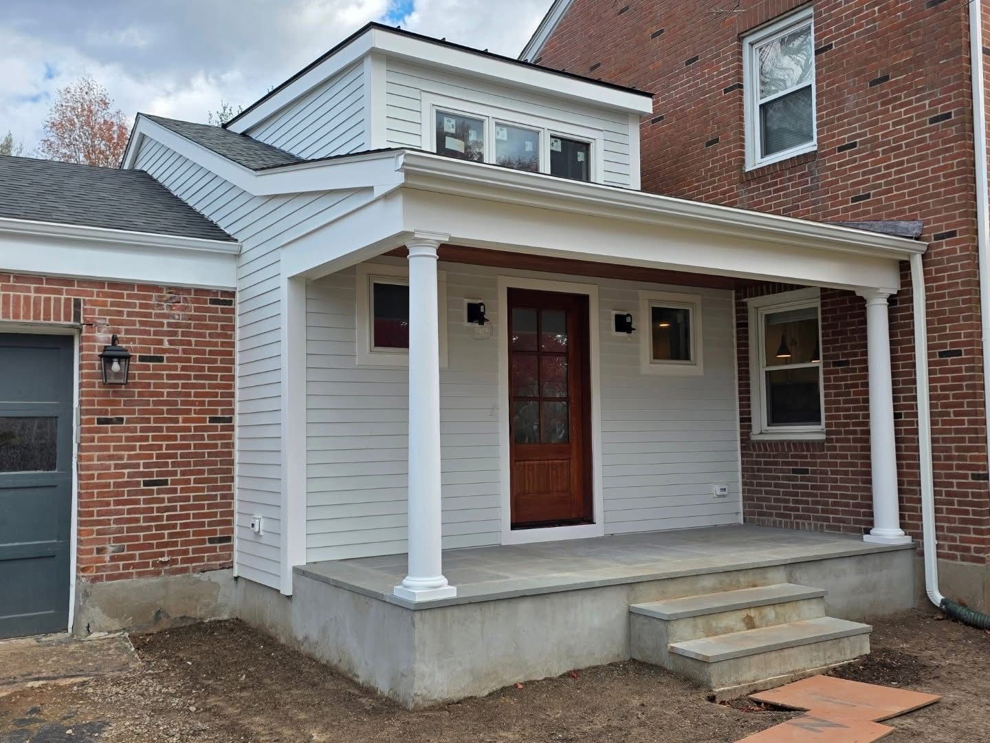 New construction: white porch addition with steps, brown door, and brick and gray walls.