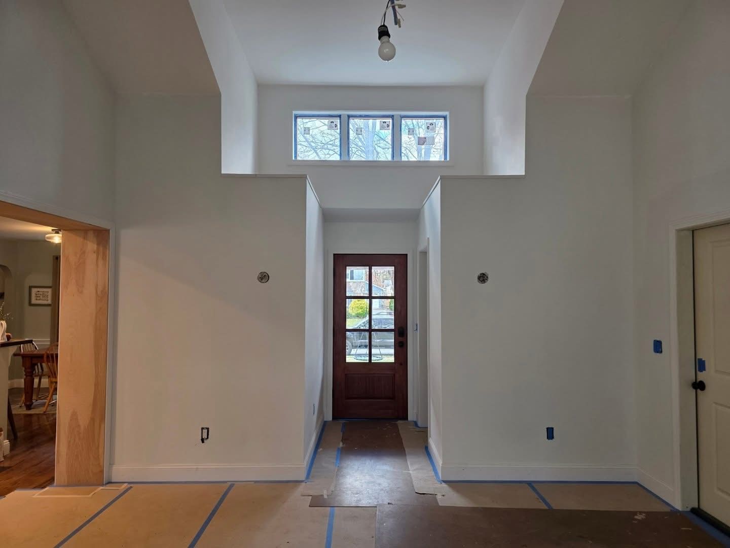 Interior view of a white-walled entryway with a brown door, window above, and exposed flooring.