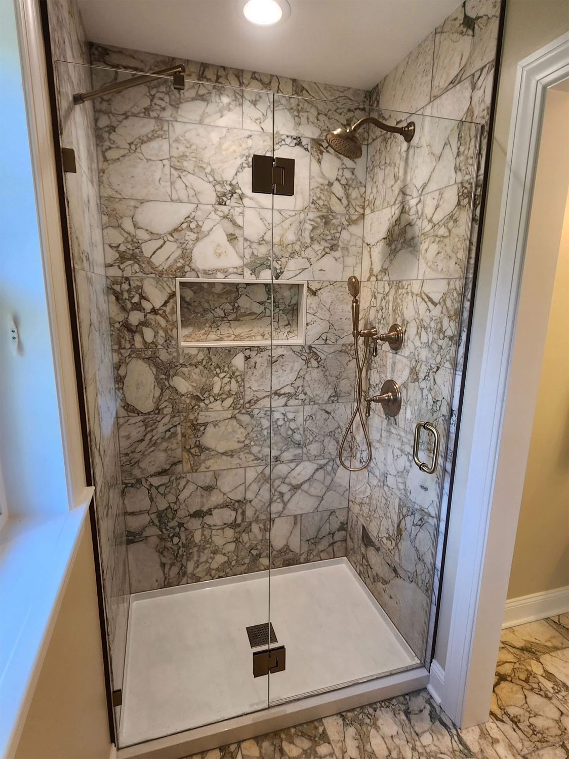 Marble-tiled shower with a built-in shelf, glass door, and bronze fixtures.