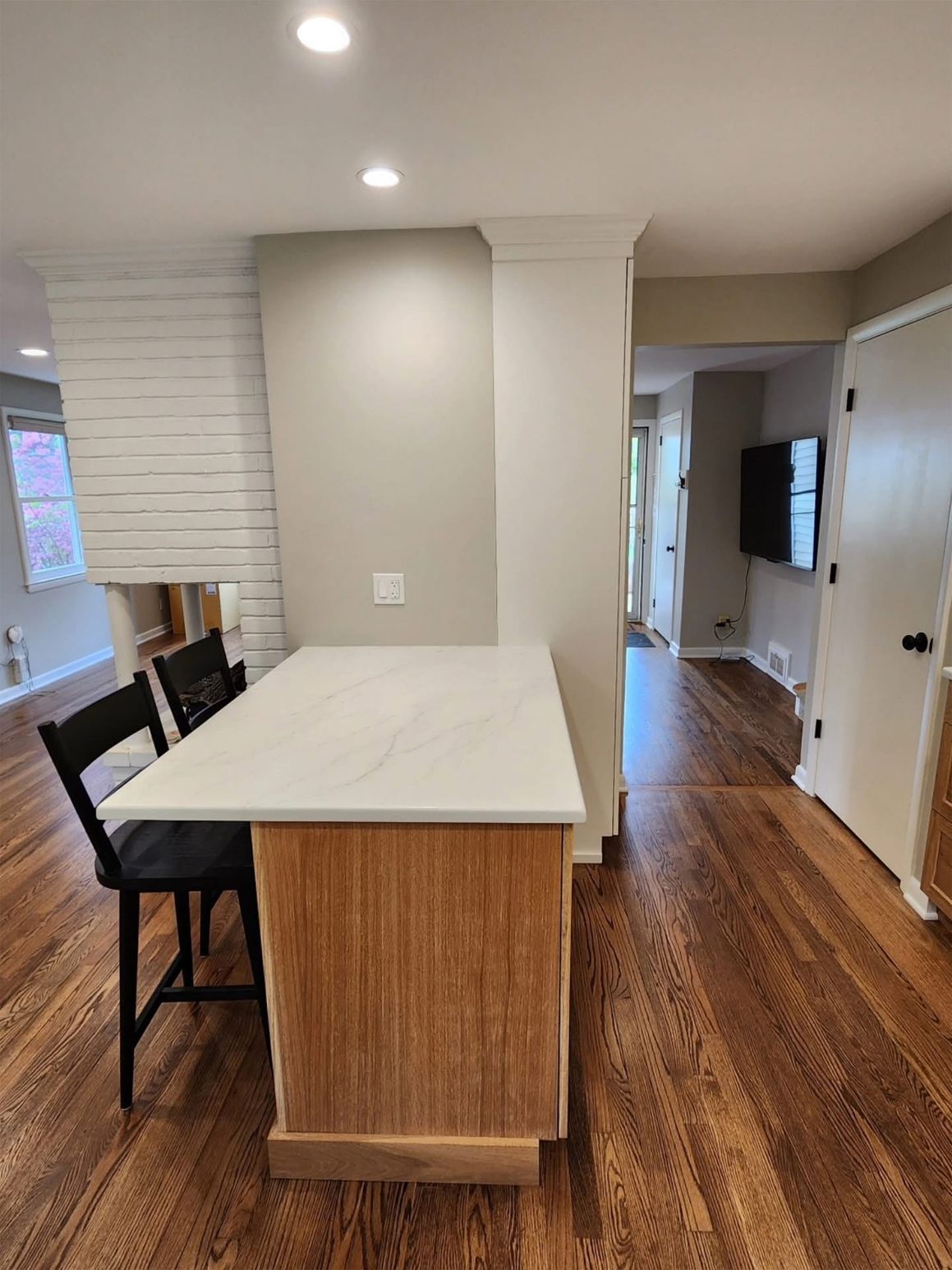 Kitchen island with white countertop, wood base, and two black chairs. Hardwood floors.