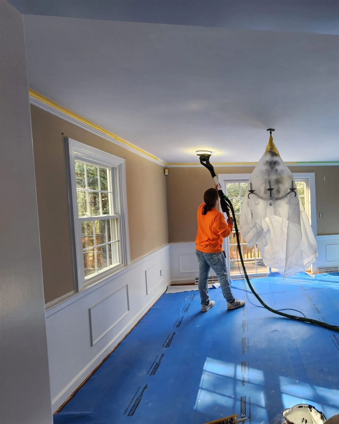 Person using a dustless sanding system on a ceiling in a room with blue floor covering and tan walls.