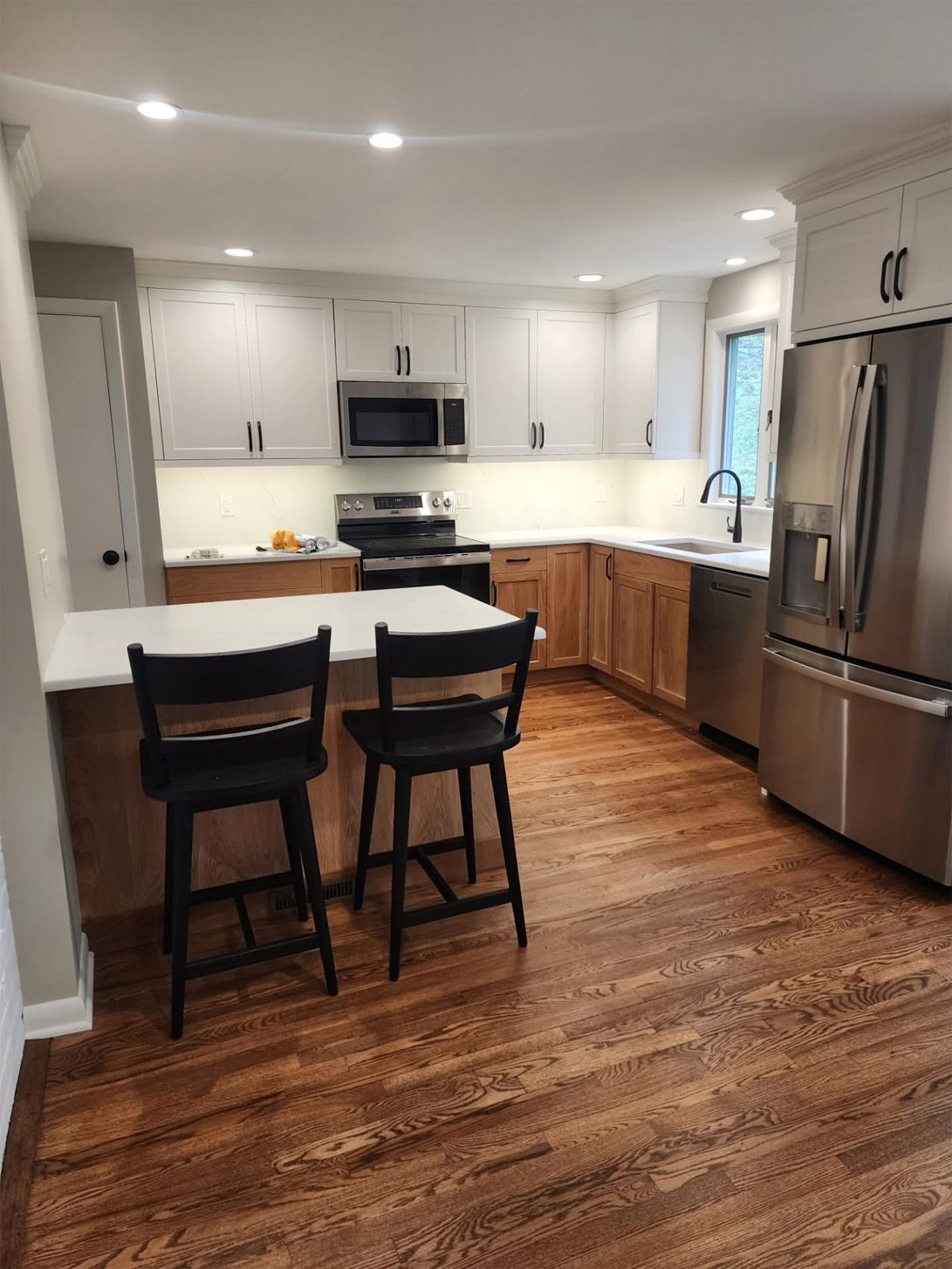 Modern kitchen with white and wood cabinets, stainless steel appliances, and two black bar stools.