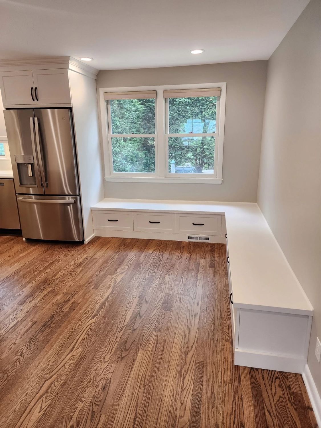 Kitchen with hardwood floor, built-in white bench under window, stainless steel fridge, and gray walls.