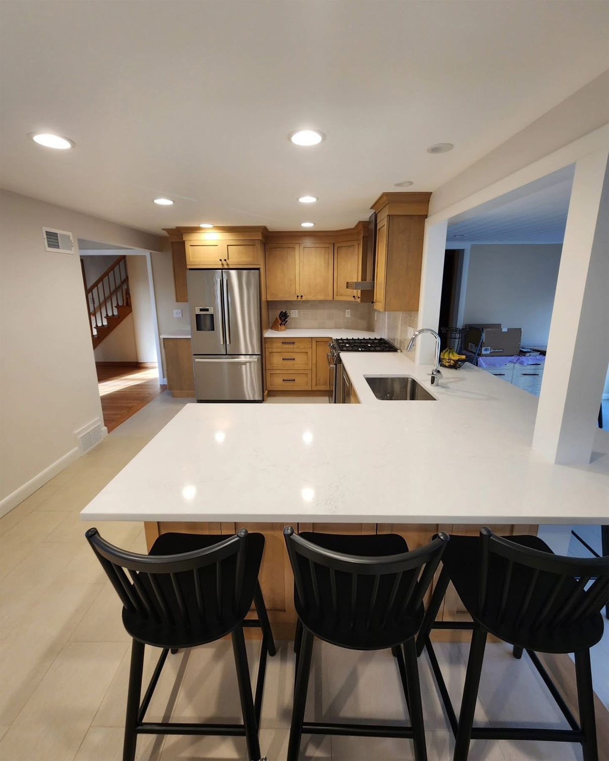 Modern kitchen with light wood cabinets, white countertops, and black bar stools.