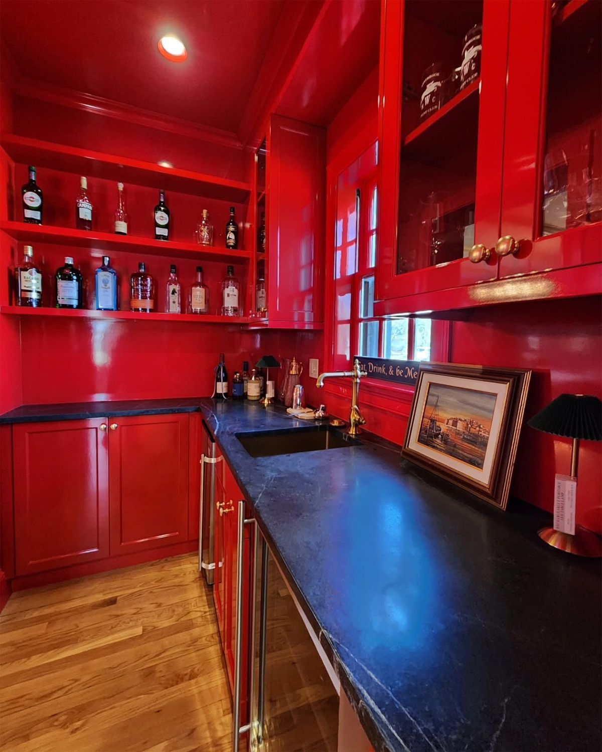Red glossy home bar with open shelves, cabinets, and black countertop.
