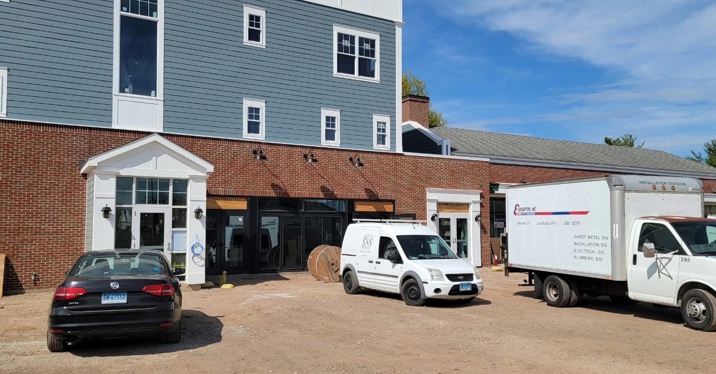 Exterior of a building with a blue facade, a brown roof, and several vehicles parked out front.