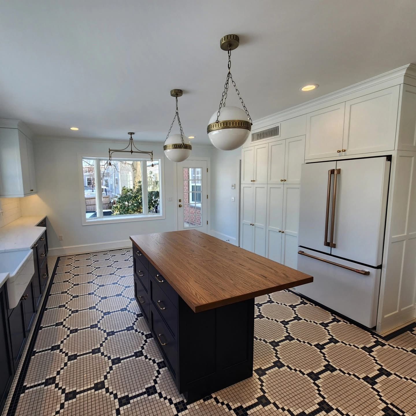 Kitchen with dark blue island, white cabinets, decorative patterned floor, and pendant lights.