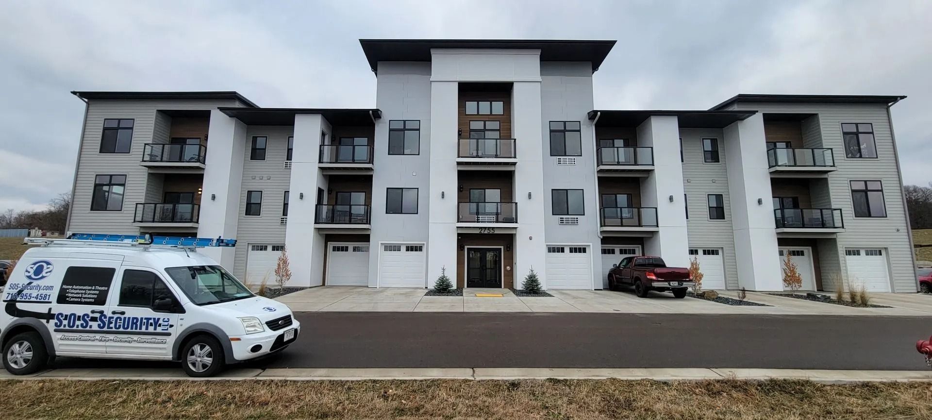 White van parked in front of a modern apartment building with balconies and garages on a cloudy day.