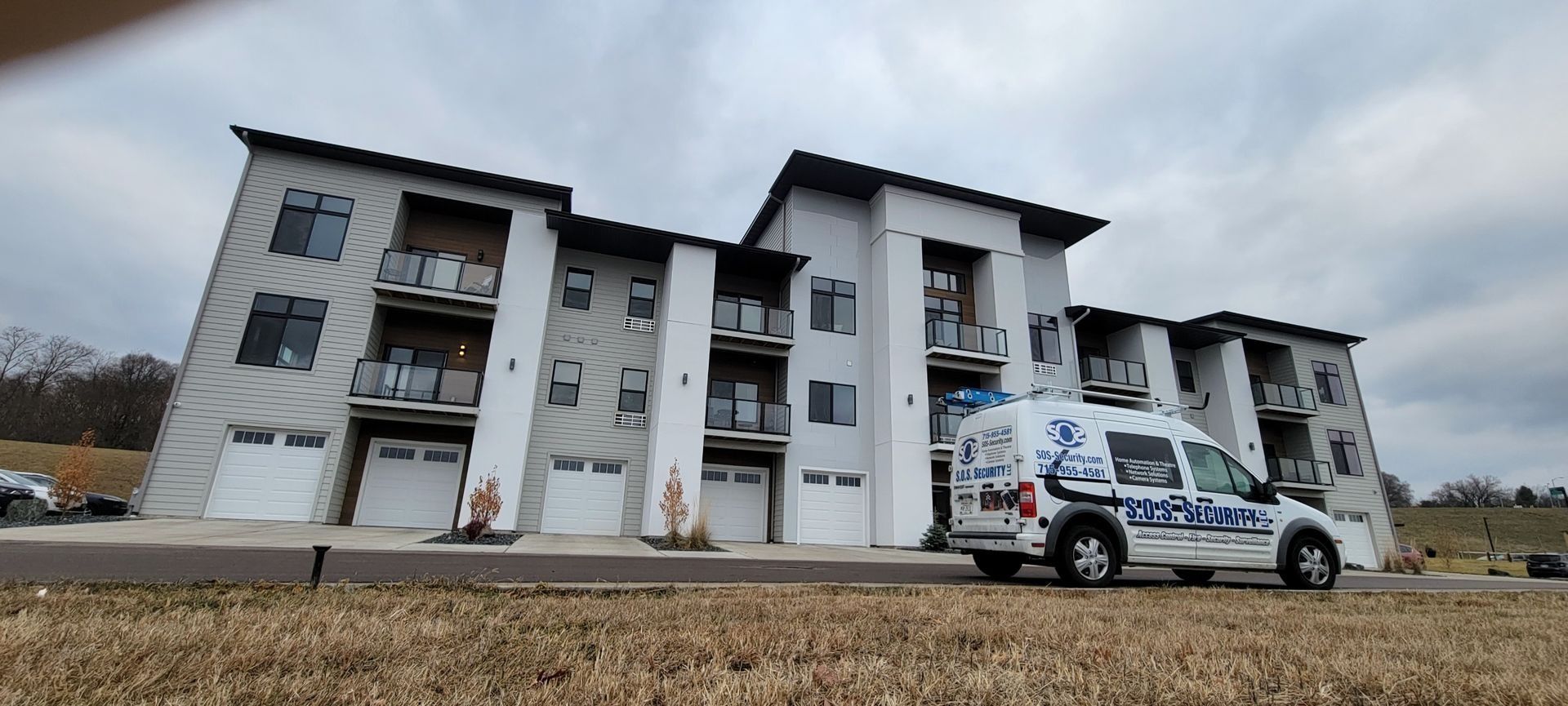 Modern apartment building with a white service van parked in front. Overcast sky.