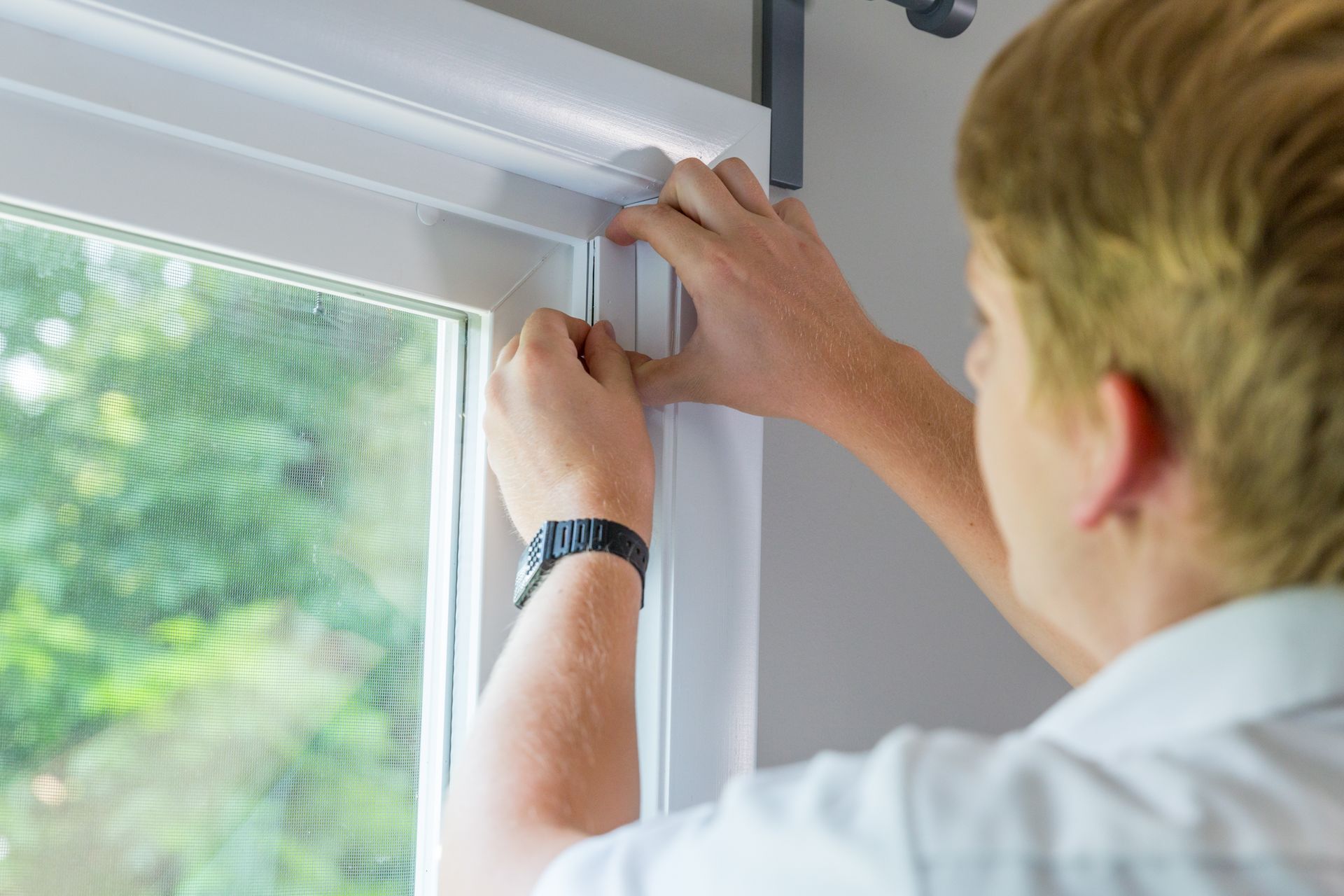 Person installing a white window trim, hands close up.
