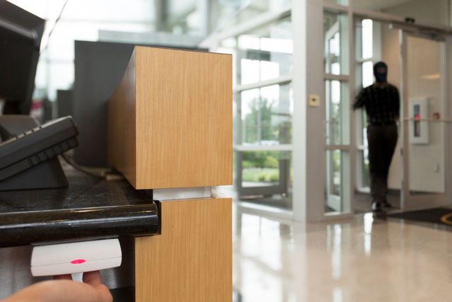 Person in black clothing exiting a building. A hand swipes a card at a reader on a counter near an entry door.