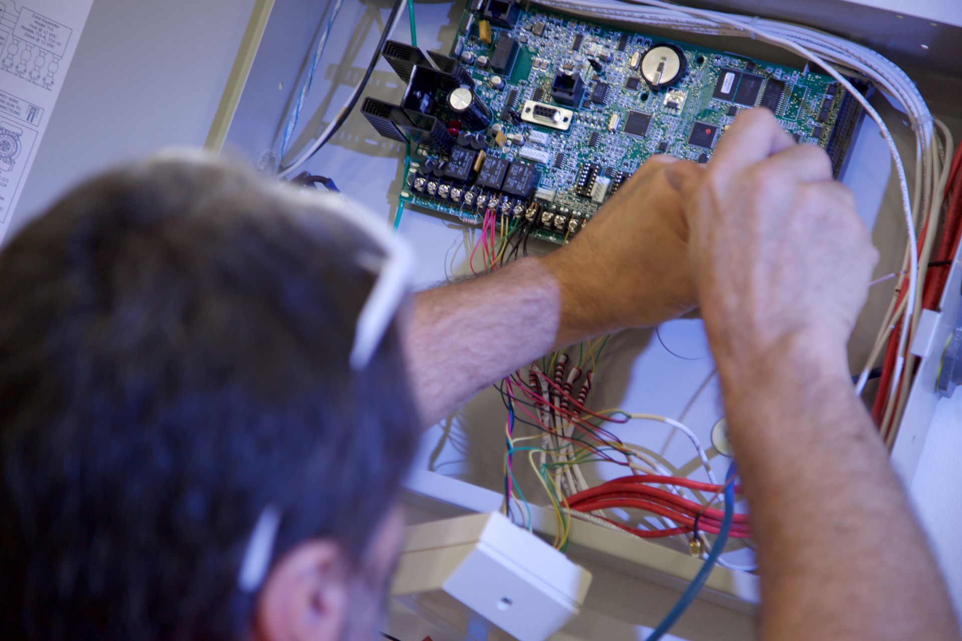 Person working on electronic circuit board inside a metal box, connecting wires.