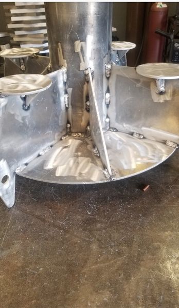 Metal assembly with a central pipe, radial fins, and circular plates, showing visible weld marks on a workshop floor.
