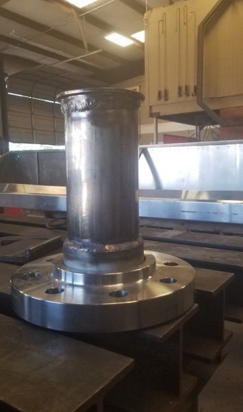 A metal pipe welded to a circular flanged base sits on a workbench in a workshop.