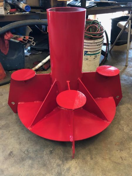 A red, custom-welded steel anchor base for a pole, featuring a central cylinder with support fins and flat circular plates.