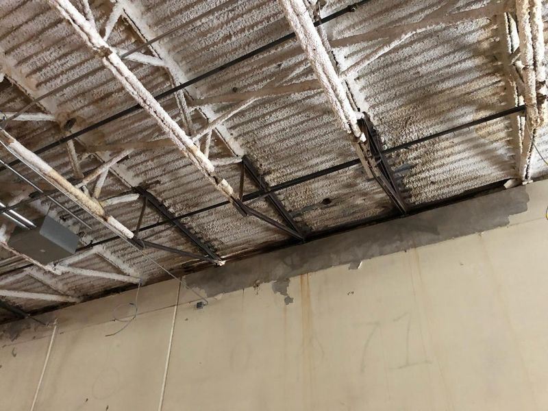 Exposed corrugated metal ceiling with steel trusses and water-stained walls in an industrial setting.