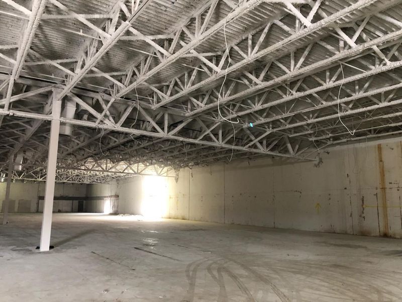 An empty, white-walled industrial warehouse space with exposed steel ceiling trusses and a concrete floor.