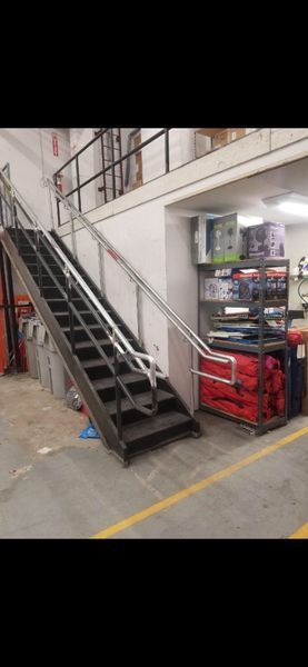 A metal staircase with a silver handrail leads to an upper platform next to a storage rack filled with supplies.