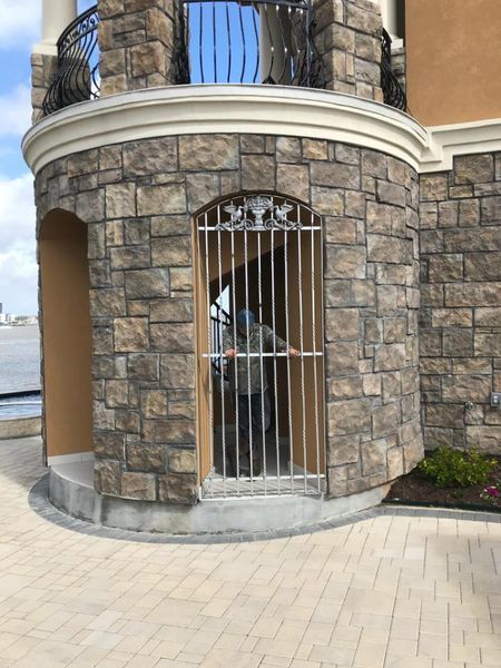 A person standing behind a metal gate inside a stone turret structure outdoors near a body of water.