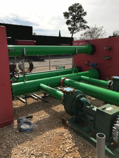 Green pipes connected to industrial pumps situated on a gravel surface between two red walls.