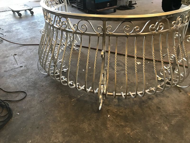 A semicircular decorative metal railing with scrollwork and twisted vertical balusters in a workshop setting.