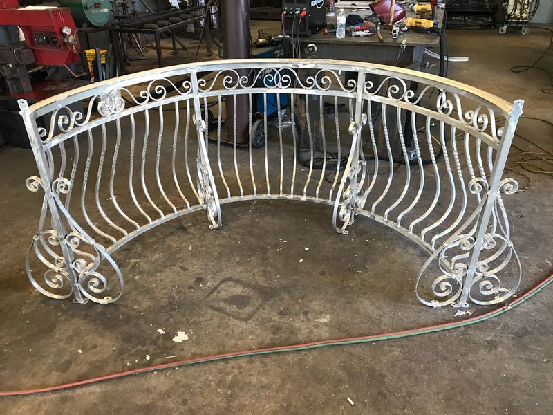 A curved, decorative silver metal railing with scrollwork designs, standing in a workshop.