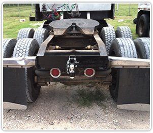 Rear view of a semi-truck showing dual wheels, a fifth-wheel hitch, mud flaps, and a towing hitch centered on the bumper.