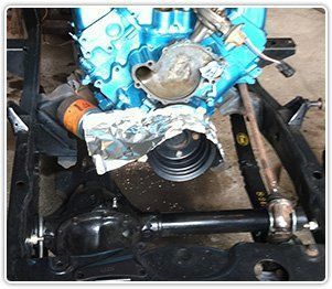 A bright blue engine sits on a black vehicle frame, with aluminum foil wrapped around the oil filter and front pulley.