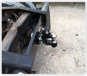 A black pintle hook hitch with a chrome ball attachment mounted to the rear frame of a truck.