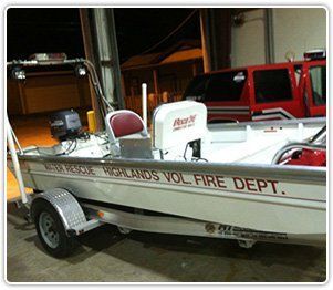 A white Highlands Volunteer Fire Department water rescue boat sits on a trailer inside a bay.