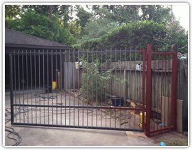 A new black metal gate installed across a driveway next to a wooden fence and a garage.