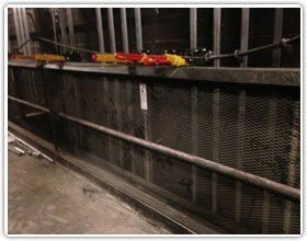 A safety railing with an attached wire mesh panel located in an industrial or mechanical space with visible piping.