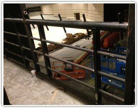 View from a black metal railing overlooking an indoor space with construction equipment, including scissor lifts.