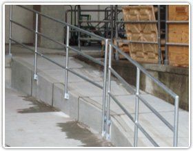 A metal handrail runs along a concrete accessibility ramp next to a loading dock area.