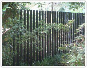 A dark vertical slat fence partially obscured by lush green garden foliage.