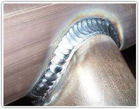 A close-up of a neat, semi-circular TIG weld bead joining two metal pipes together.