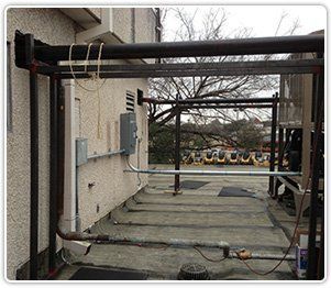 A rooftop view of a building exterior with steel framing, piping, electrical conduit, and a mechanical cooling unit.