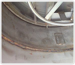 A close-up of a circular metal access hatch welded onto a large industrial tank, showing surface discoloration.