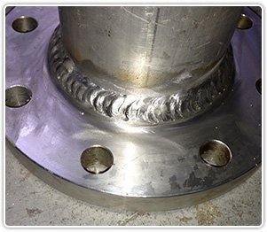A close-up of a circular stainless steel metal flange welded to a pipe, showing the consistent, rippled weld bead.