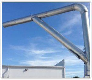 A galvanized metal structural support bracket against a blue sky, mounted above a white wall.