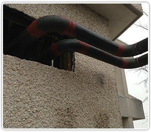 Two black pipes with red joints extend from a gap in a textured exterior building wall.
