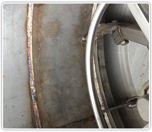 Close-up of a stainless steel tank showing a circular hatch frame, welded joints, and internal mechanical hardware.