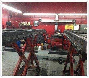 A pair of red scissor-style vehicle lifts in an auto repair shop with a red wall and a rolling tool cabinet in the back.