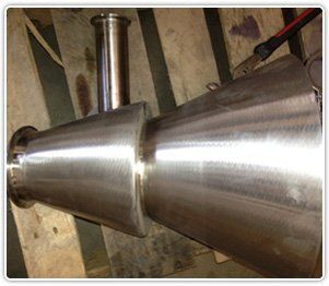 A polished metal industrial component with two conical sections and a perpendicular pipe fitting, resting on wooden slats.