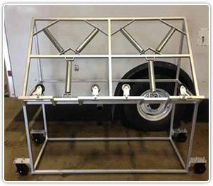 A silver metal rack on wheels featuring two top-mounted spring-loaded hold-down mechanisms for equipment.