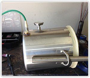 A stainless steel cylinder with a green hose, a valve, and a handle, resting on a cluttered workbench.