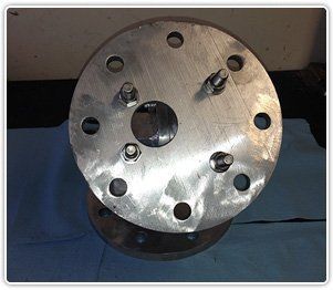 A circular metal industrial flange with multiple bolt holes and four protruding bolts on a blue surface.