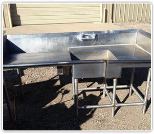 A stainless steel commercial sink with a basin on the right and a flat prep area on the left, set on a metal frame.