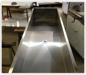 A long, rectangular, stainless steel industrial sink with a center drain, located in a workshop.